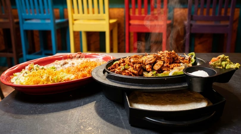 Sizzling chicken fajitas with rice, beans, guacamole, sour cream, and tortillas on a table.