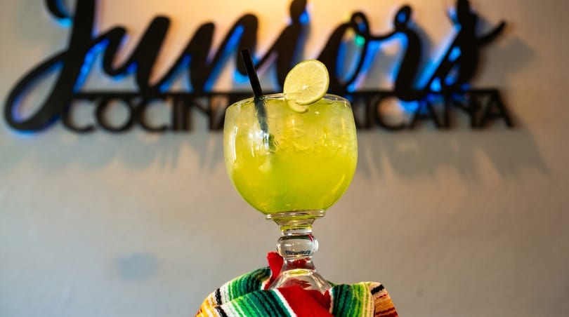 A large margarita with a lime slice and straw, resting on a colorful striped blanket.