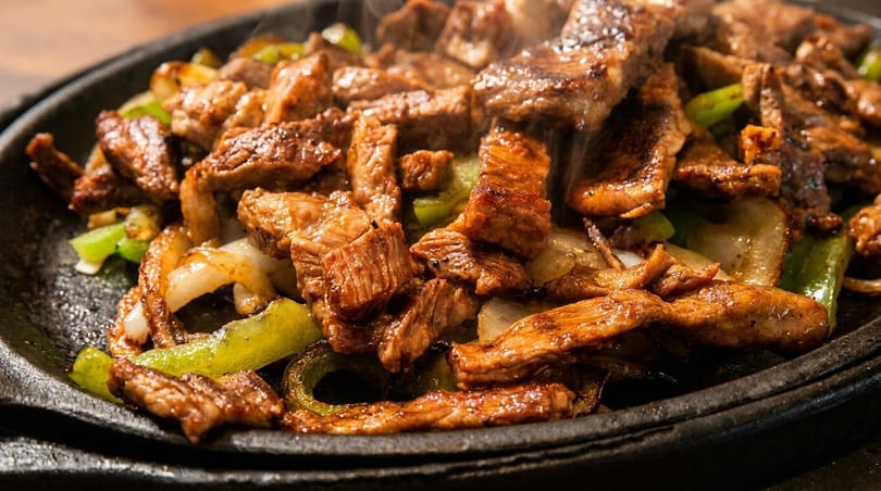 Sizzling steak fajitas with green peppers and onions on a hot cast iron plate.