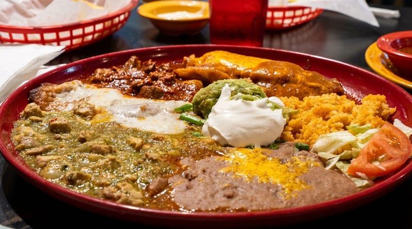 A large red plate filled with a variety of Mexican dishes, including rice, beans, and meats.