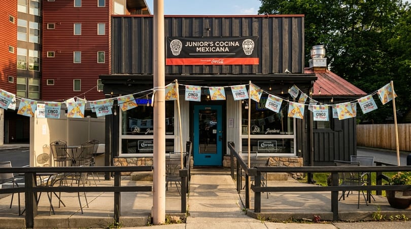 Junior's Cocina Mexicana restaurant exterior with outdoor seating, a blue door, and festive Cinco de Mayo banners.
