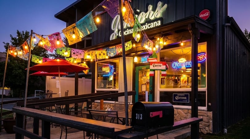 Juniors Cocina Mexicana restaurant exterior at dusk, adorned with colorful papel picado and string lights.